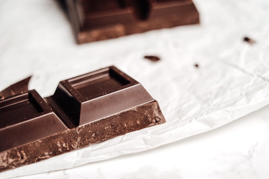 Broken dark chocolate bar pieces on crinkled white foil wrapper, close-up macro shot